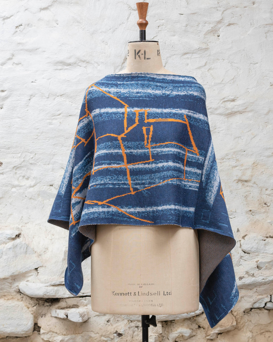 A blue poncho with orange linear design, a statement piece of contemporary knitwear by Nielanell, Shetland, displayed on a mannequin.
