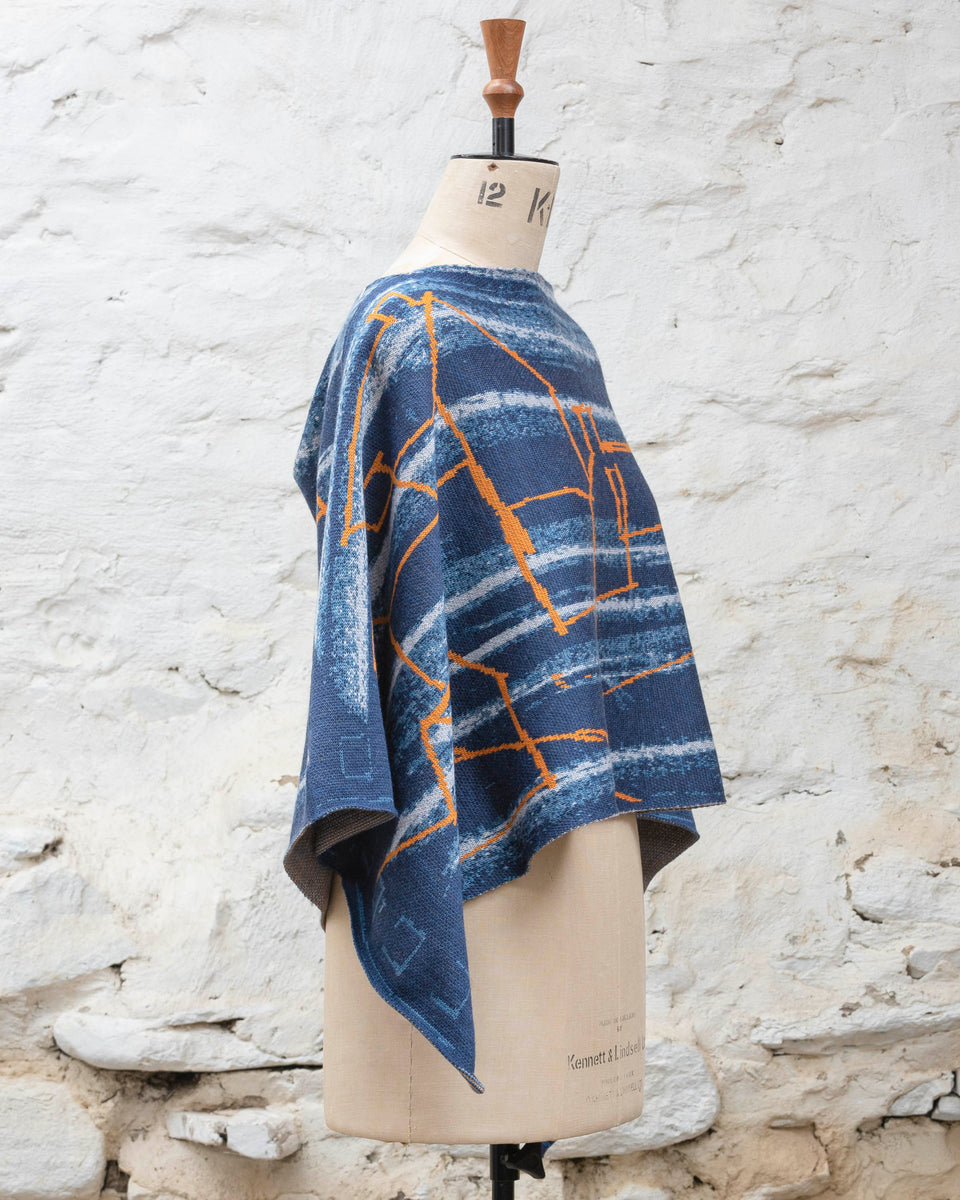 A blue poncho with orange linear pattern, a statement piece of contemporary knitwear by Nielanell, Shetland, displayed on a mannequin.