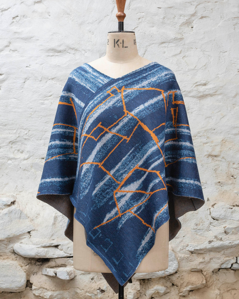 A blue poncho with orange linear design, a statement piece of contemporary knitwear by Nielanell, Shetland, displayed on a mannequin.