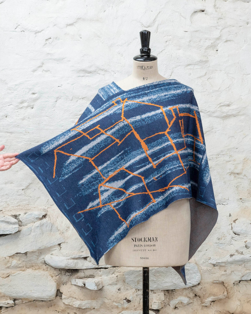 A blue poncho with orange linear design, a statement piece of contemporary knitwear by Nielanell, Shetland, displayed on a mannequin.