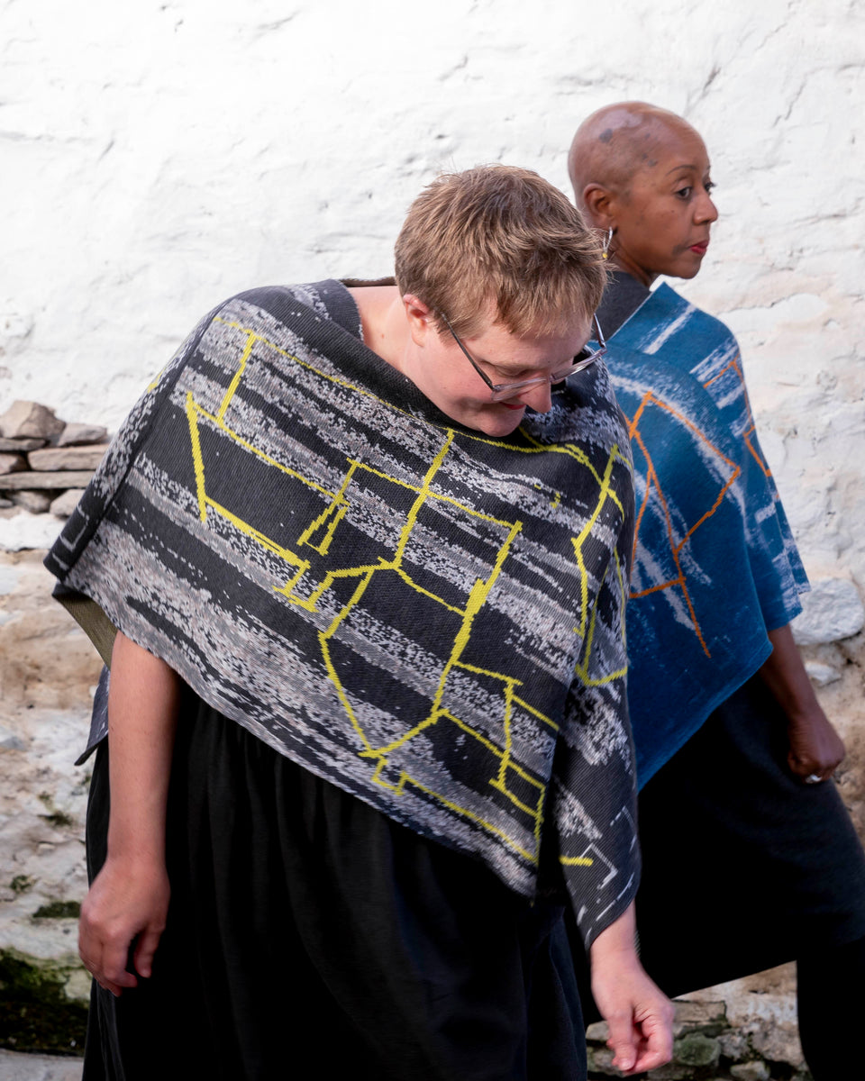 Two women wear punk influenced knitwear in greys and blues with neon yellow and orange highlights. Contemporary Scottish design