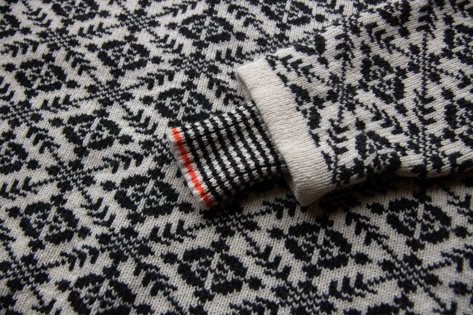 Fair Isle sweater in charcoal and pale grey. Detail of stripey inset cuff with orange highlight stripe.