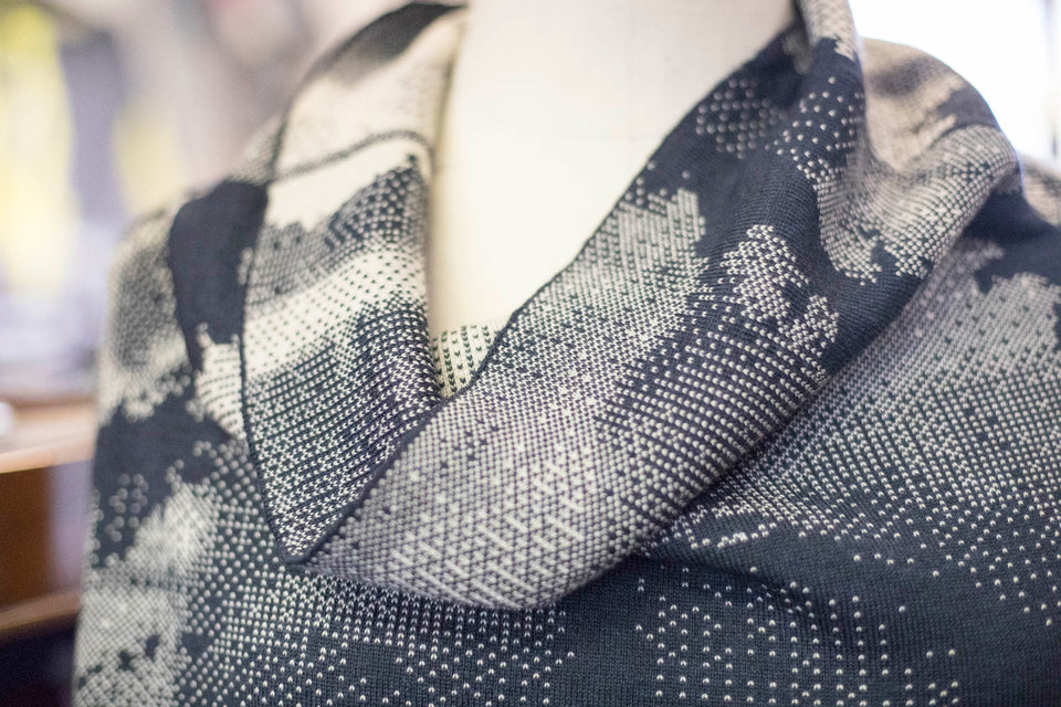 Knitted Rani jumper. Small abstract patterns make up a larger design with photographic imagery. Shown in inky blue and antique white. Cowl neck detail