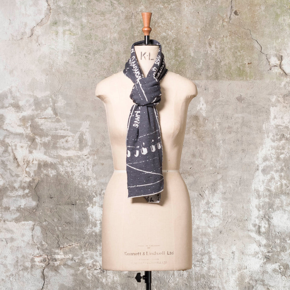 Knitted Byre cravat. A small shawl scarf with an abstract, graphic design in an asymmetric shape. Shown in Charcoal and stone white