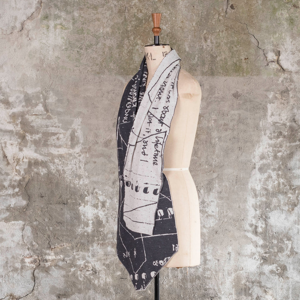 Knitted Byre cravat. A small shawl scarf with an abstract, graphic design in an asymmetric shape. Shown in Charcoal and stone white