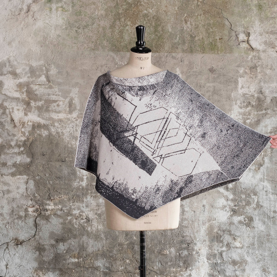 Knitted Byre cape. Abstract, graphic design in an asymmetric shape. Shown in Charcoal and stone white