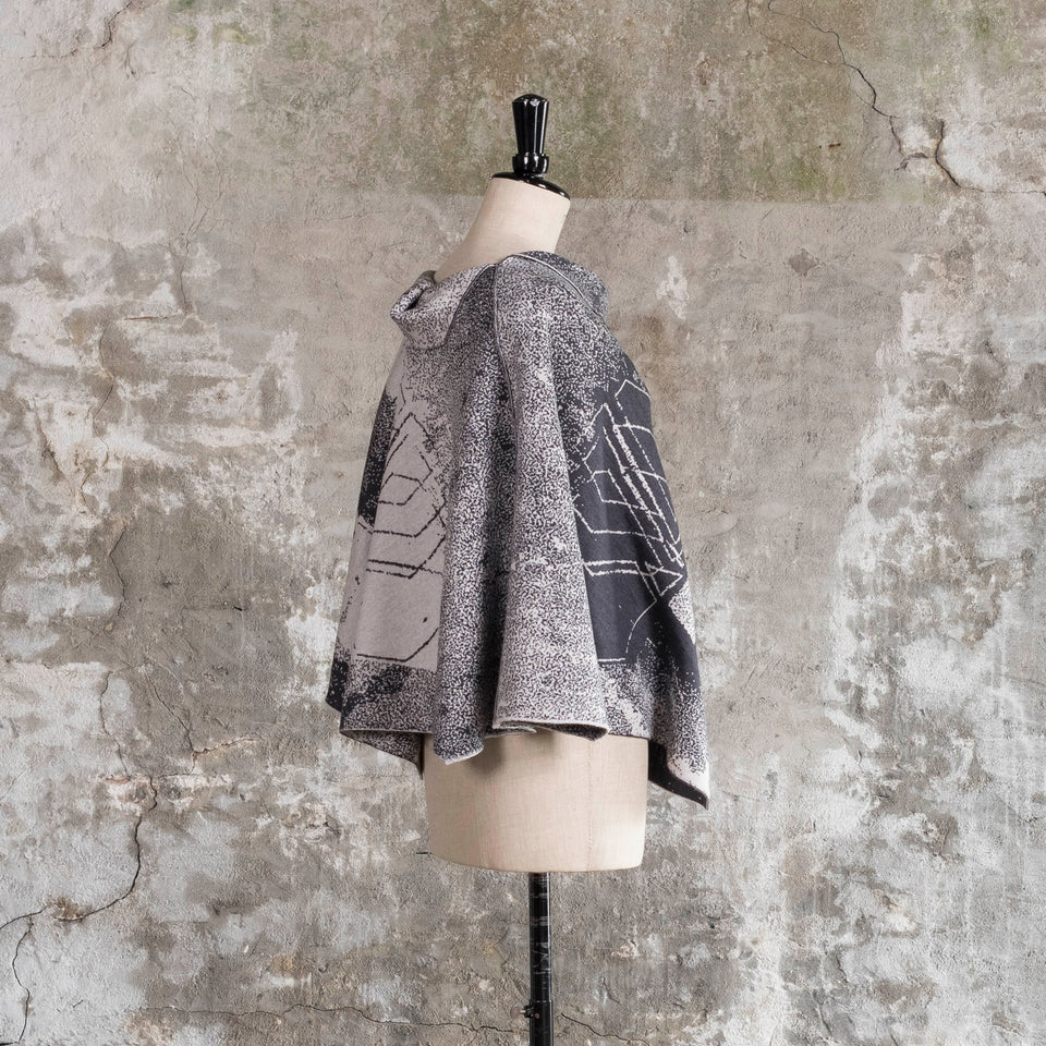 Knitted Byre cape. Abstract, graphic design in an asymmetric shape. Shown in Charcoal and stone white