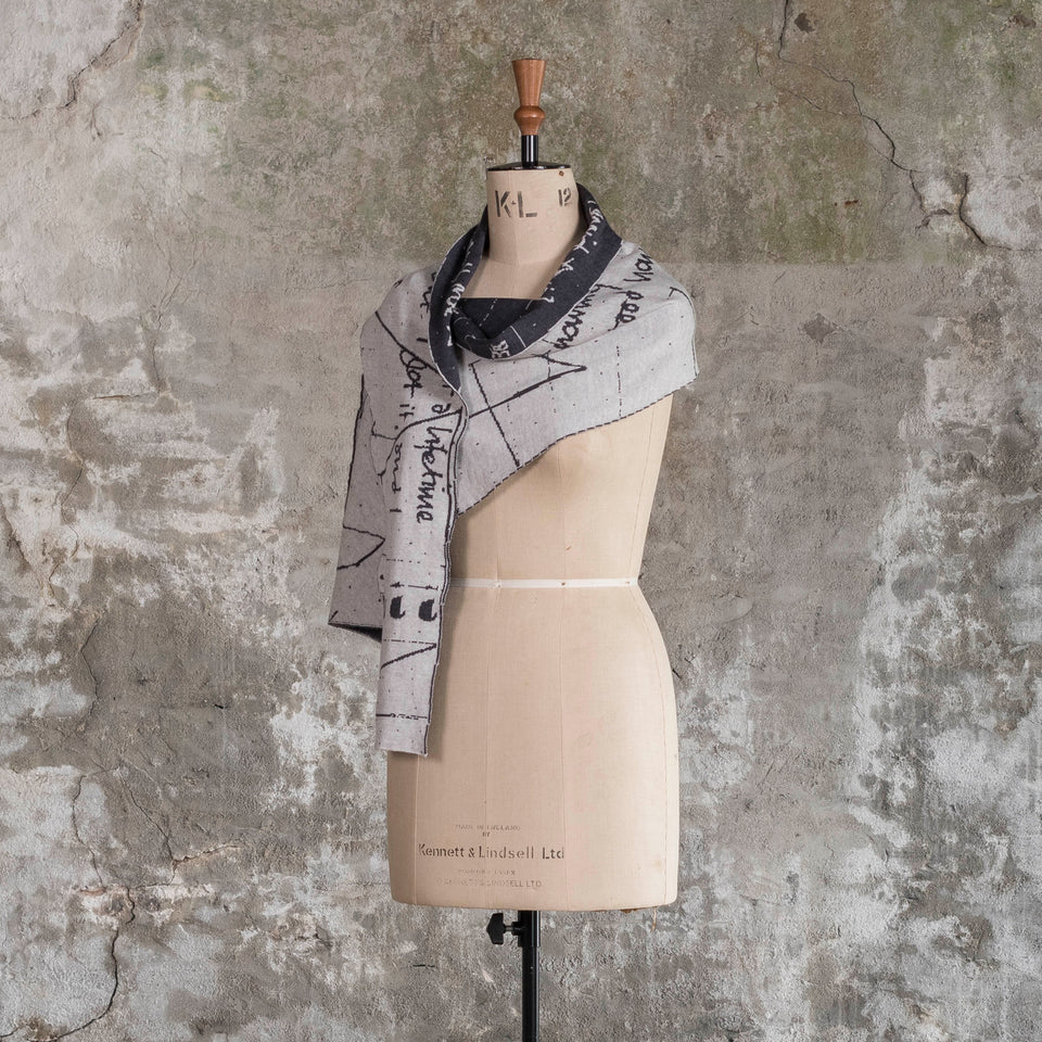 Knitted Byre cravat. A small shawl scarf with an abstract, reversible graphic design in an asymmetric shape. Shown in Charcoal and stone white