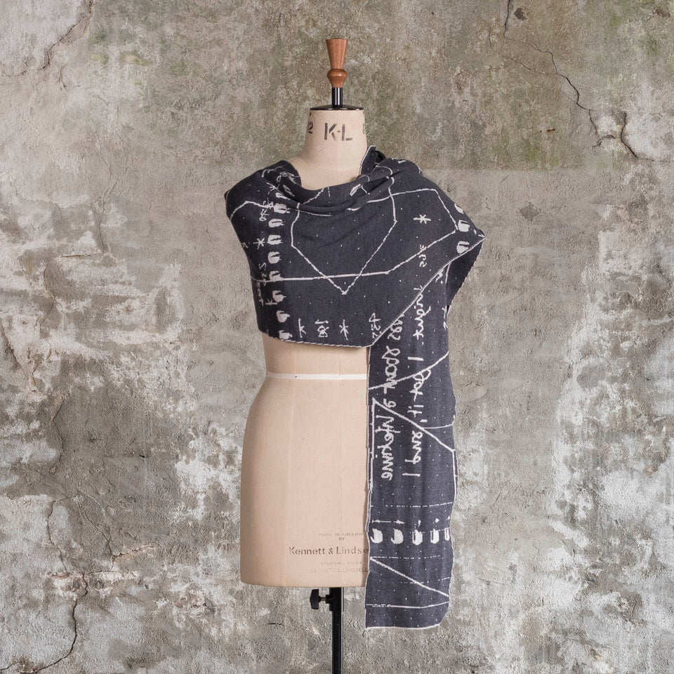 Knitted Byre cravat. A small shawl scarf with an abstract, graphic design in an asymmetric shape. Shown in Charcoal and stone white
