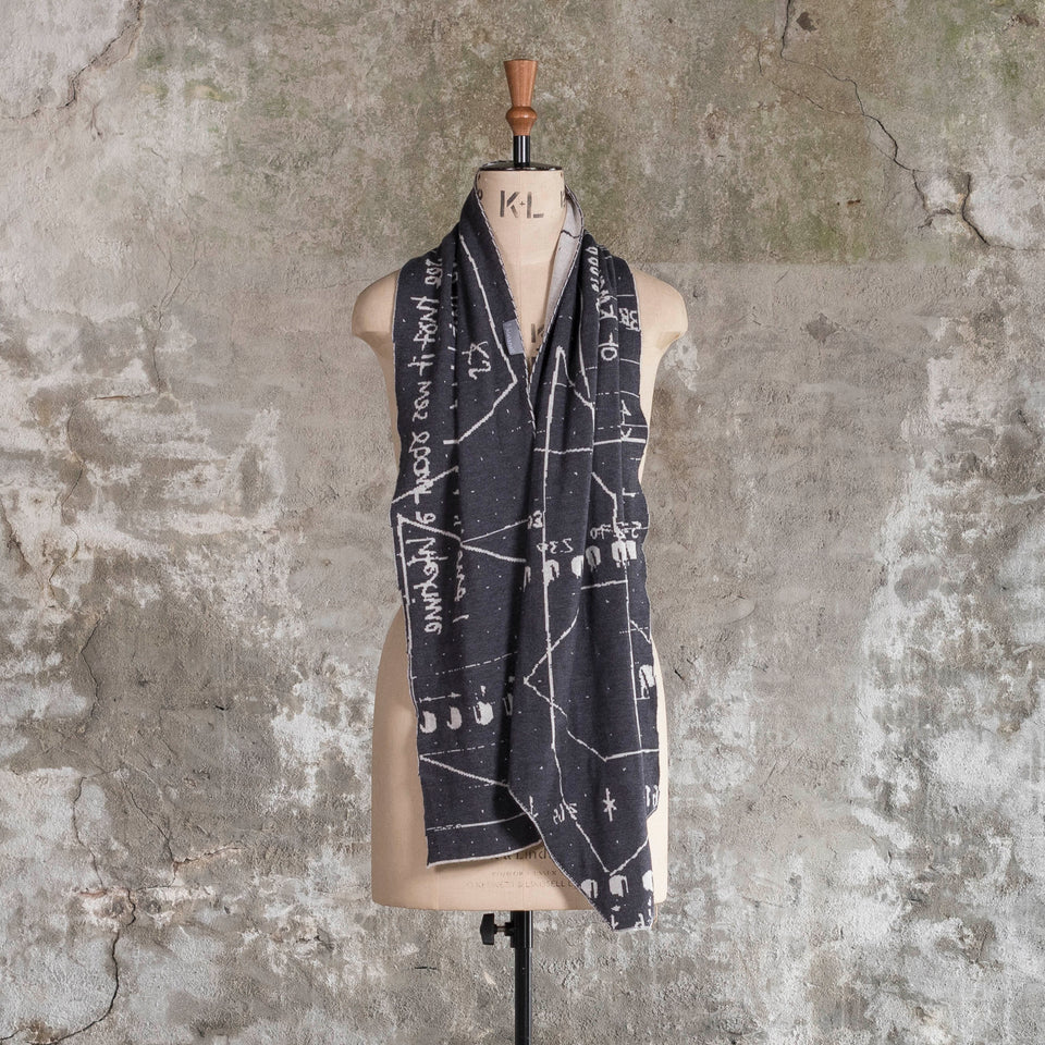 Knitted Byre cravat. A small shawl scarf with an abstract, graphic design in an asymmetric shape. Shown in Charcoal and stone white