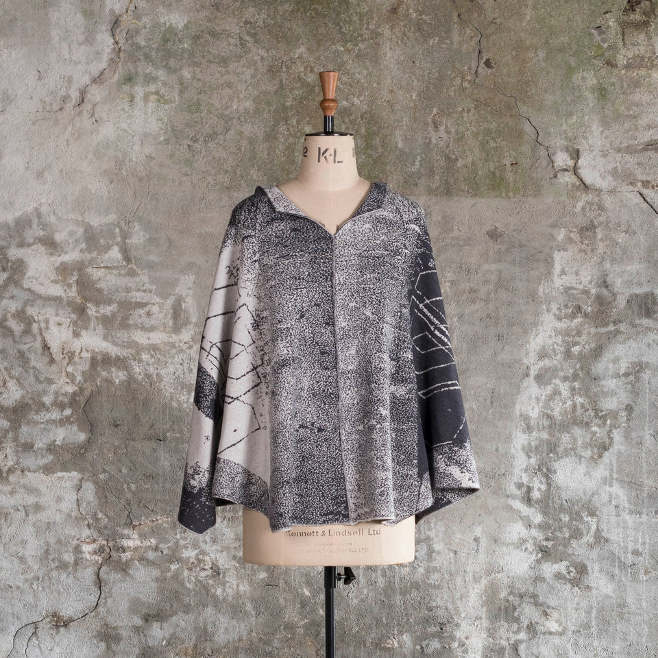 Knitted Byre cape. Abstract, graphic design in an asymmetric shape. Shown in Charcoal and stone white