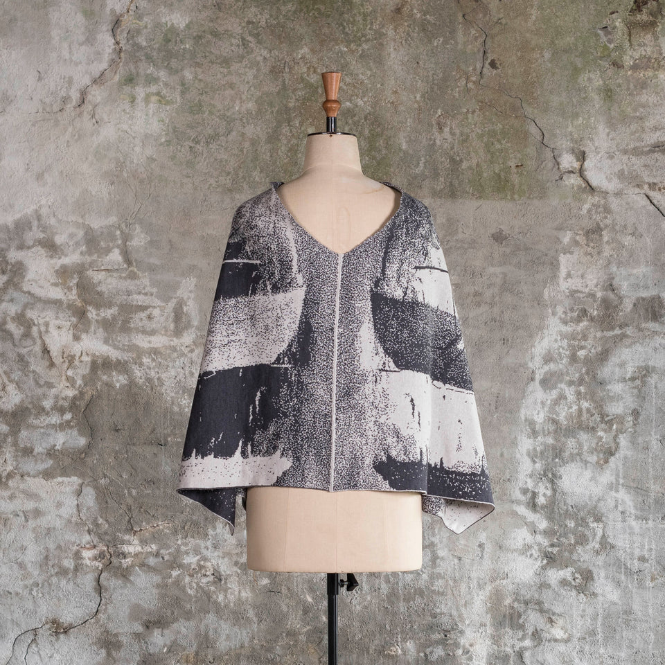Knitted Byre cape. Abstract, graphic design in an asymmetric shape. Shown in Charcoal and stone white