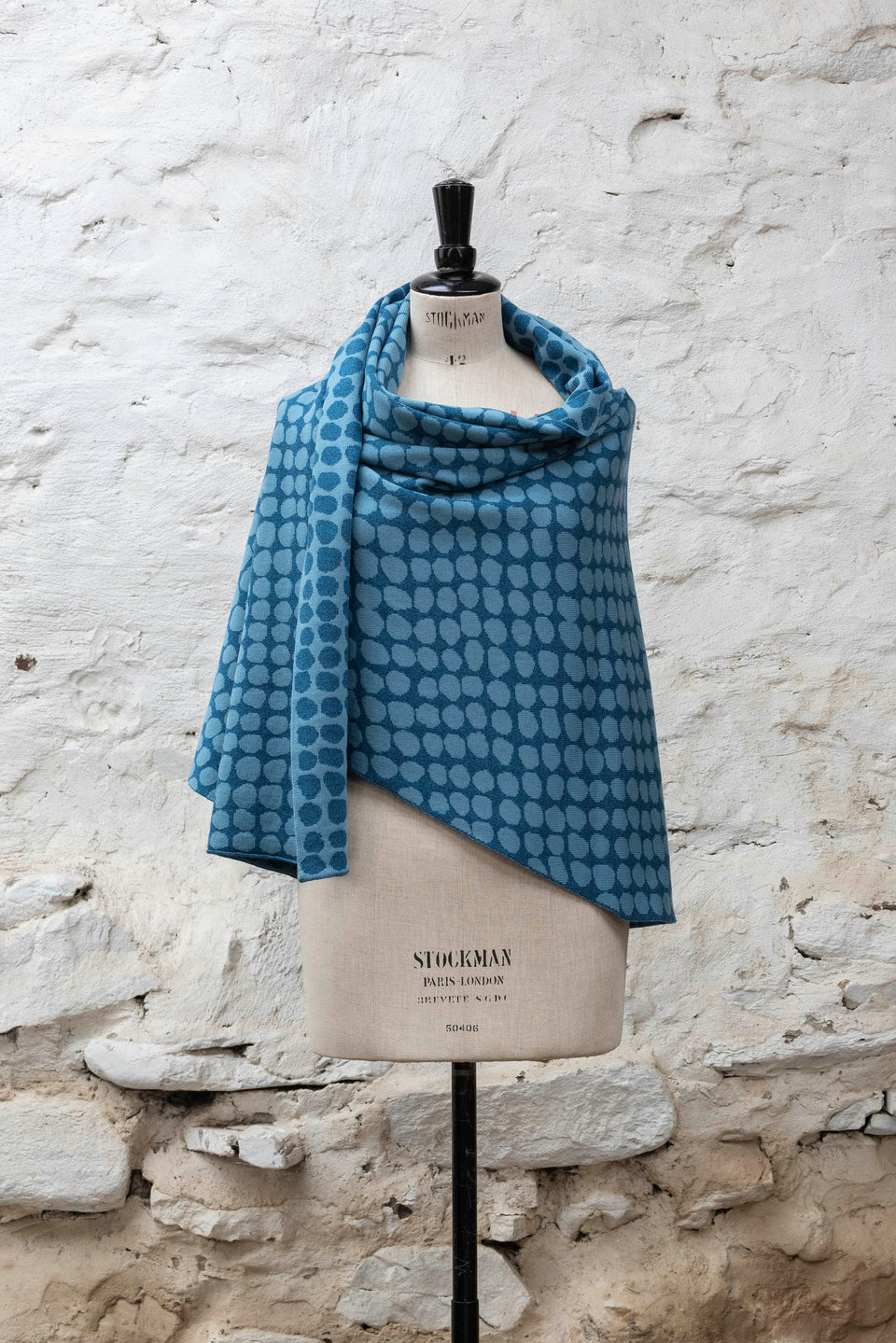 Knitted ebb-stanes wrap with irregular dot pattern shown in blues