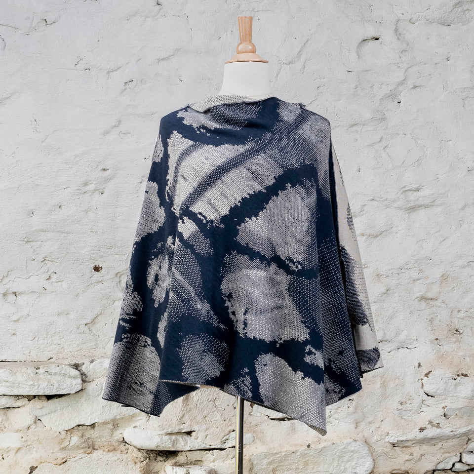 Knitted Rani cape. Small abstract patterns make up a larger design with photographic imagery. Shown in inky blue and antique white