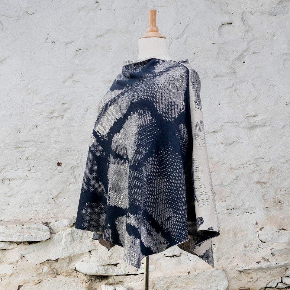 Knitted Rani cape. Small abstract patterns make up a larger design with photographic imagery. Shown in inky blue and antique white