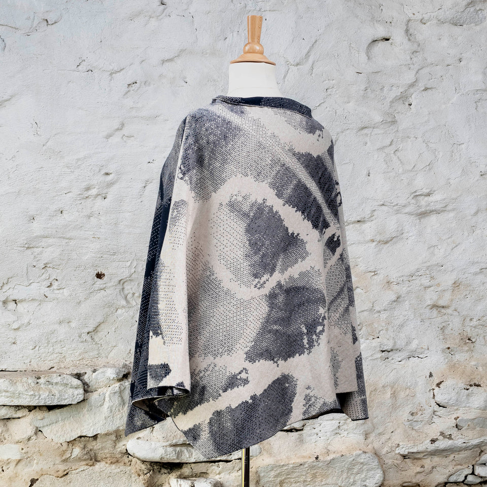 Knitted Rani cape. Small abstract patterns make up a larger design with photographic imagery. Shown in inky blue and antique white