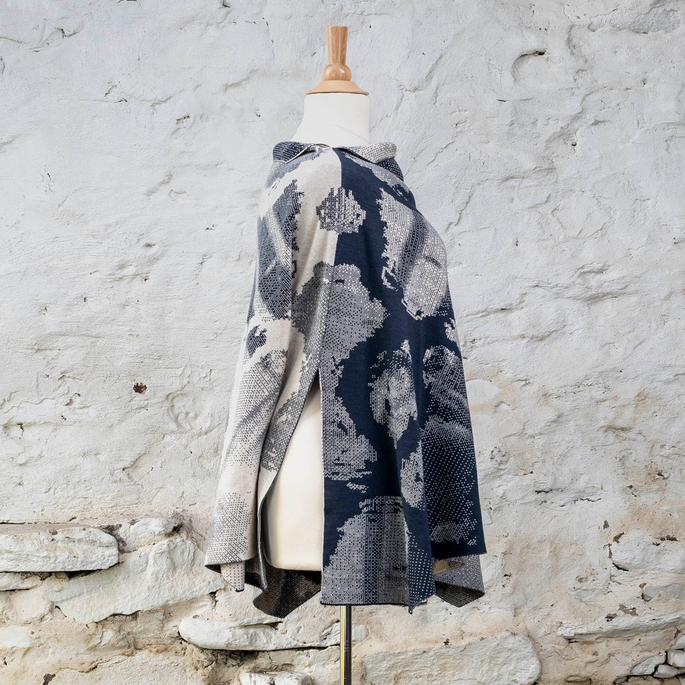 Knitted Rani cape. Small abstract patterns make up a larger design with photographic imagery. Shown in inky blue and antique white