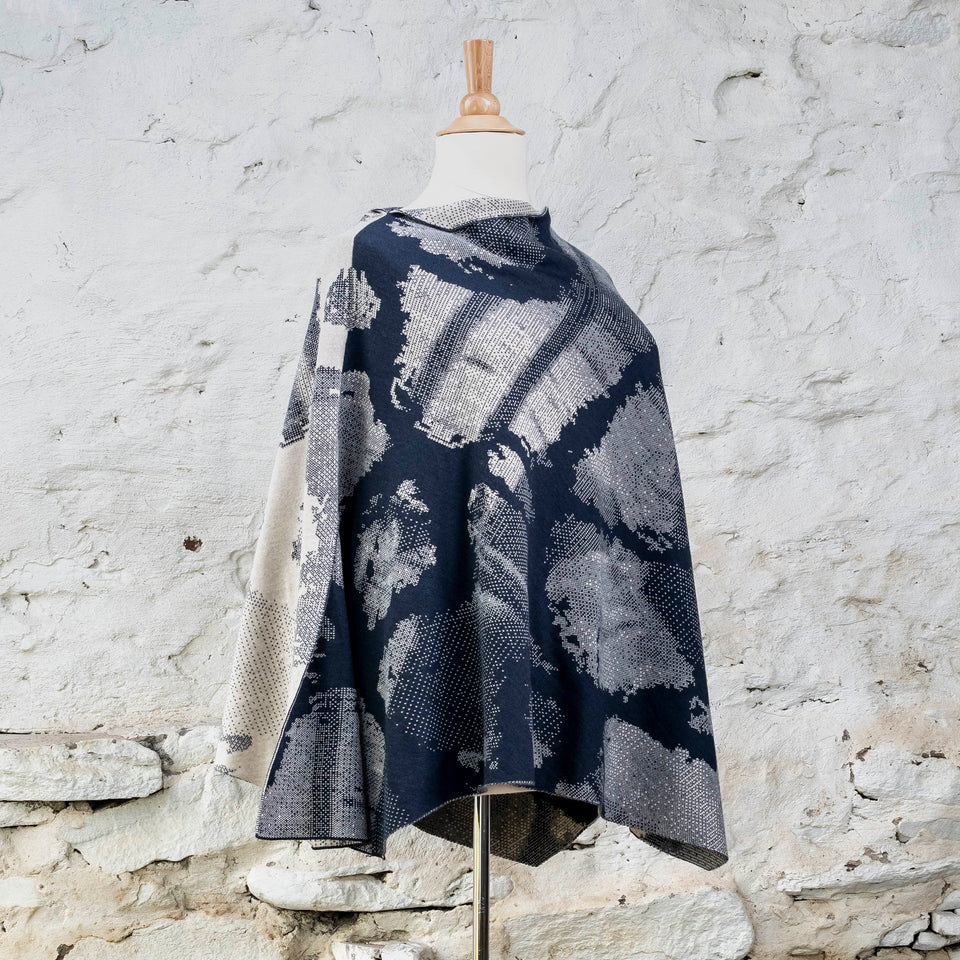 Knitted Rani cape. Small abstract patterns make up a larger design with photographic imagery. Shown in inky blue and antique white