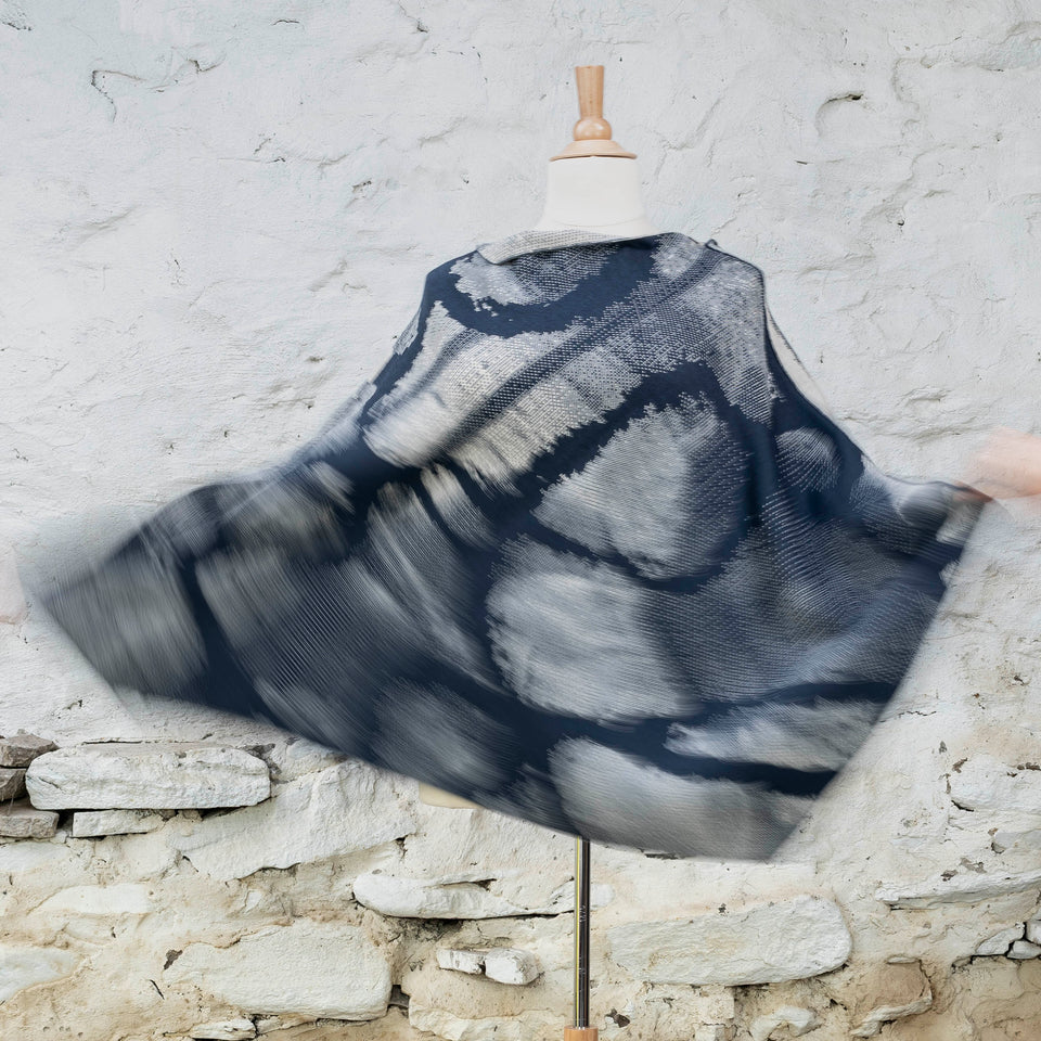 Knitted Rani cape. Small abstract patterns make up a larger design with photographic imagery. Shown in inky blue and antique white