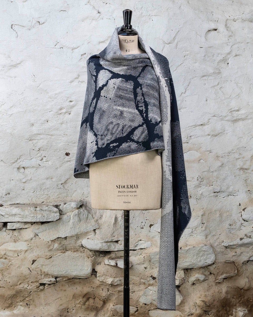 Knitted Rani shawl / wrap. Small abstract patterns make up a larger design with photographic imagery. Shown in inky blue and antique white