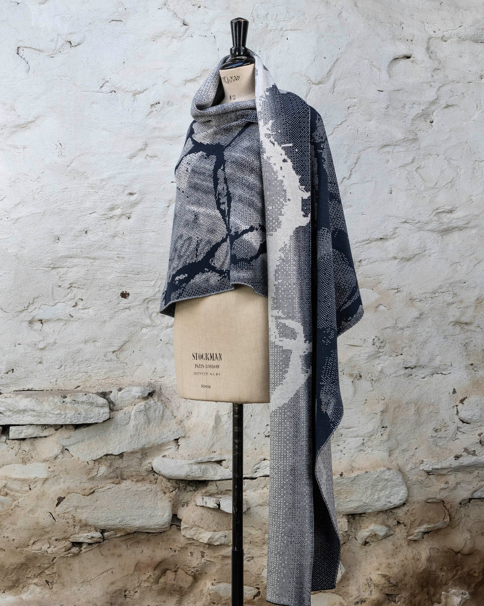 Knitted Rani shawl / wrap. Small abstract patterns make up a larger design with photographic imagery. Shown in inky blue and antique white