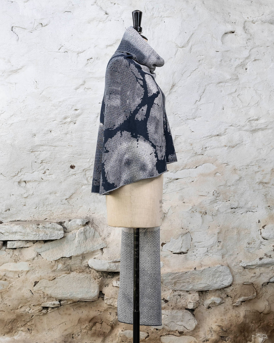 Knitted Rani shawl / wrap. Small abstract patterns make up a larger design with photographic imagery. Shown in inky blue and antique white