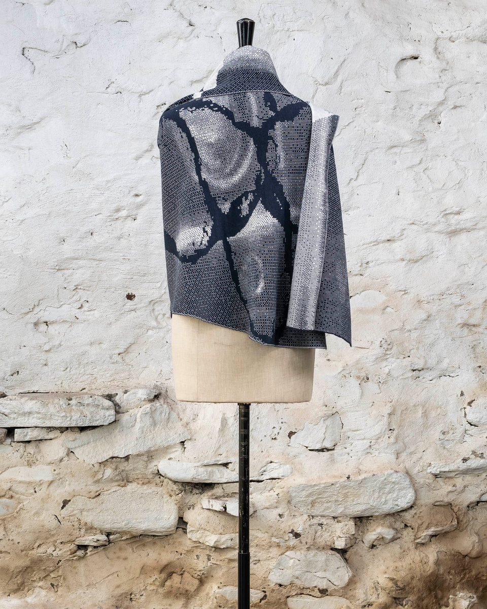 Knitted Rani shawl / wrap. Small abstract patterns make up a larger design with photographic imagery. Shown in inky blue and antique white