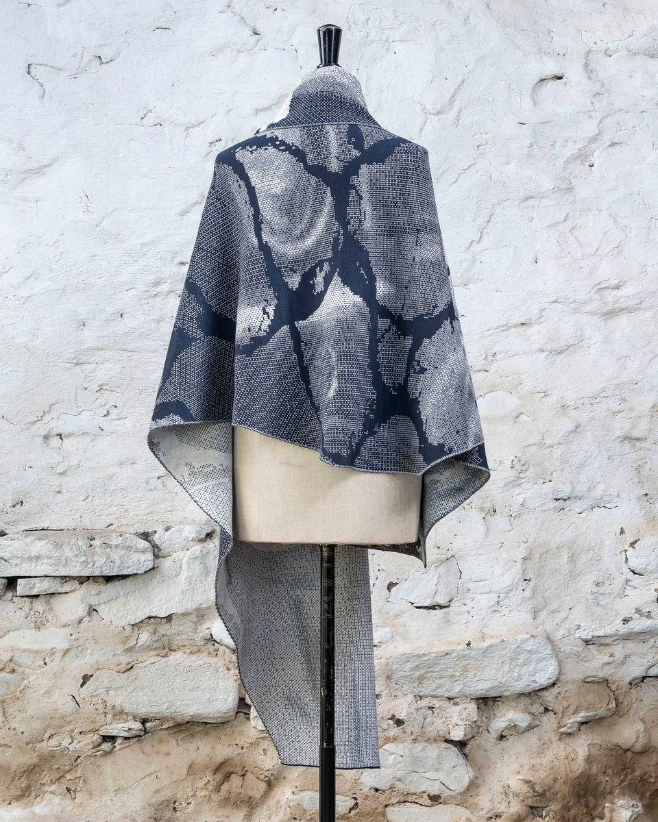 Knitted Rani shawl / wrap. Small abstract patterns make up a larger design with photographic imagery. Shown in inky blue and antique white