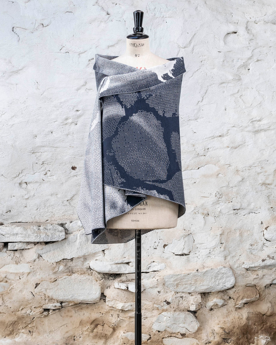 Knitted Rani shawl / wrap. Small abstract patterns make up a larger design with photographic imagery. Shown in inky blue and antique white