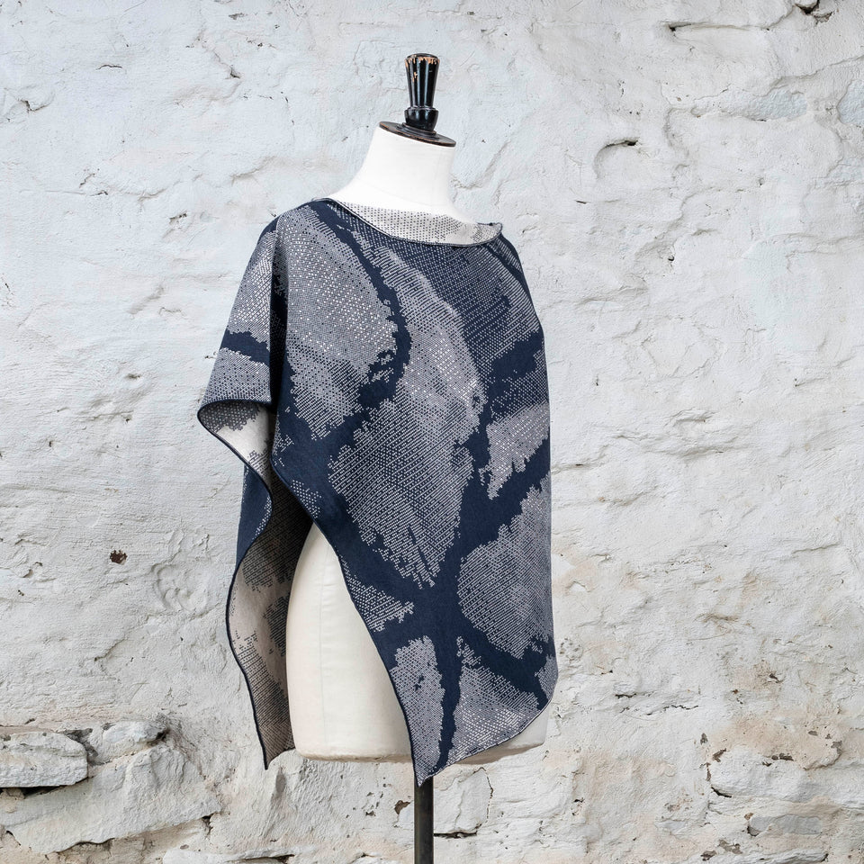 Knitted Rani shorter cape. Small abstract patterns make up a larger design with photographic imagery. Shown in inky blue and antique white