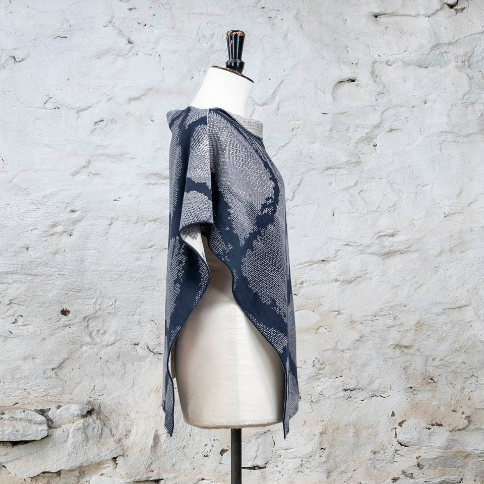 Knitted Rani shorter cape. Small abstract patterns make up a larger design with photographic imagery. Shown in inky blue and antique white