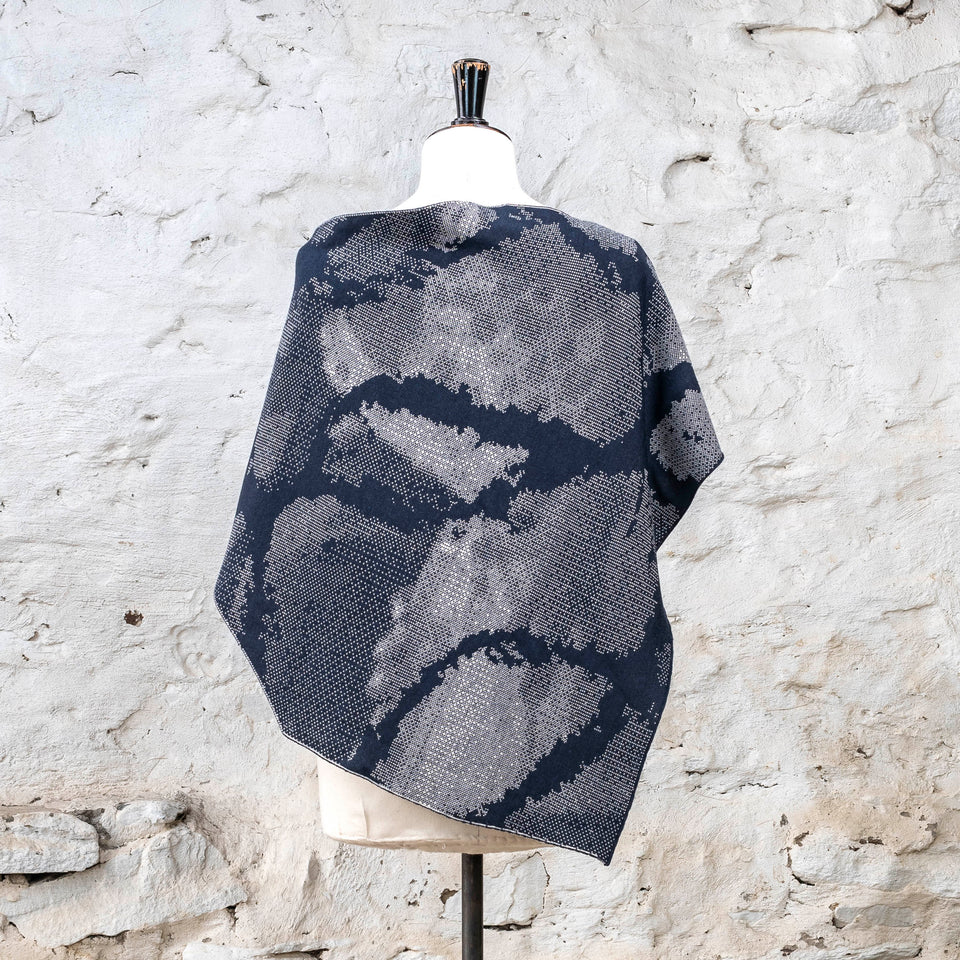 Knitted Rani shorter cape. Small abstract patterns make up a larger design with photographic imagery. Shown in inky blue and antique white