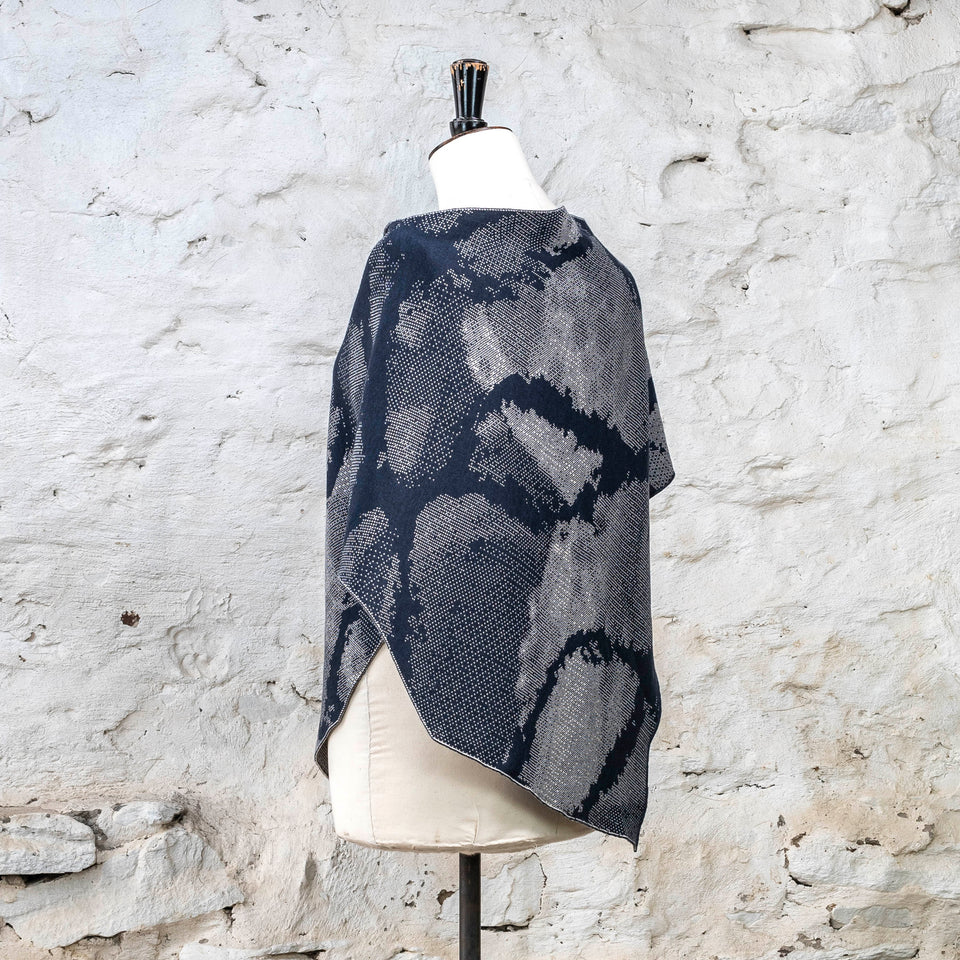 Knitted Rani shorter cape. Small abstract patterns make up a larger design with photographic imagery. Shown in inky blue and antique white