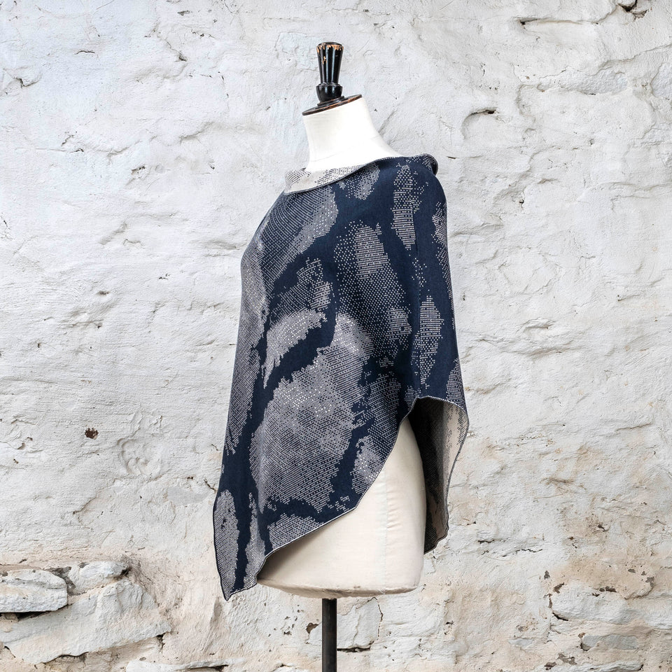 Knitted Rani shorter cape. Small abstract patterns make up a larger design with photographic imagery. Shown in inky blue and antique white