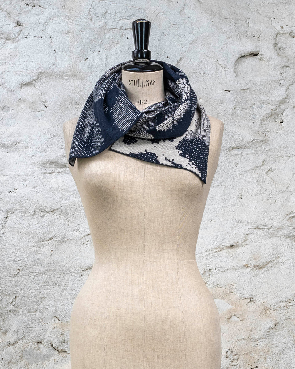 Knitted Rani scarf. Small abstract patterns make up a larger design with photographic imagery. Shown in inky blue and antique white
