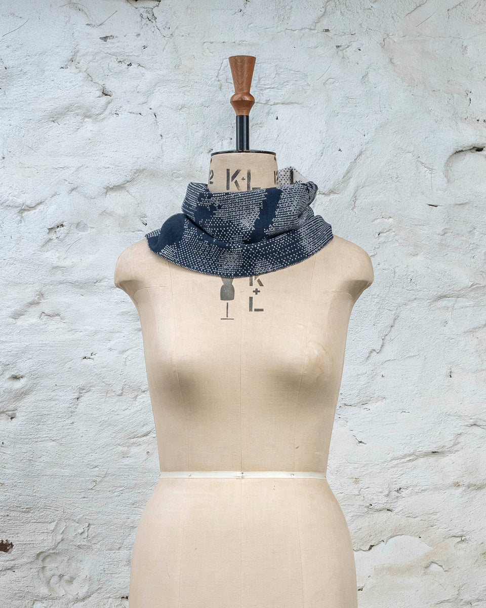 Knitted Rani asymmetric cowl. Small abstract patterns make up a larger design with photographic imagery. Shown in inky blue and antique white
