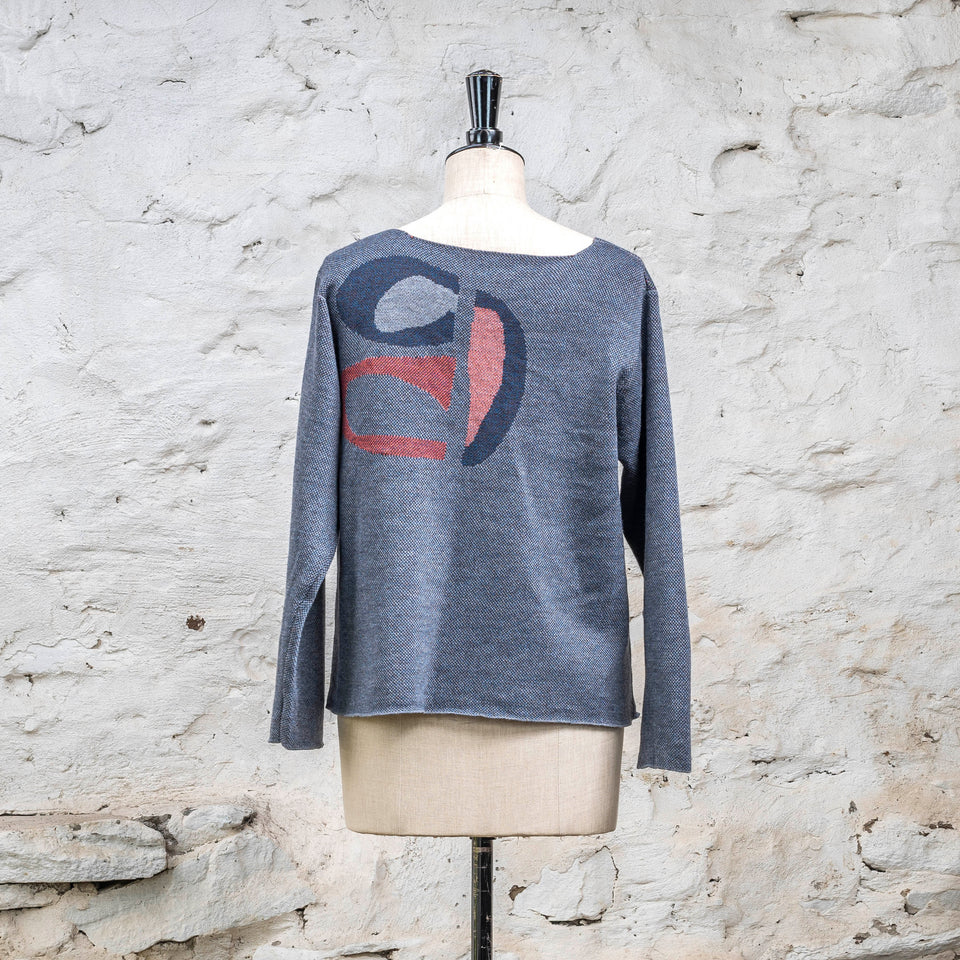 View of the back of Scottish contemporary knitted jumper in blues with accents in coral. The pattern is abstract