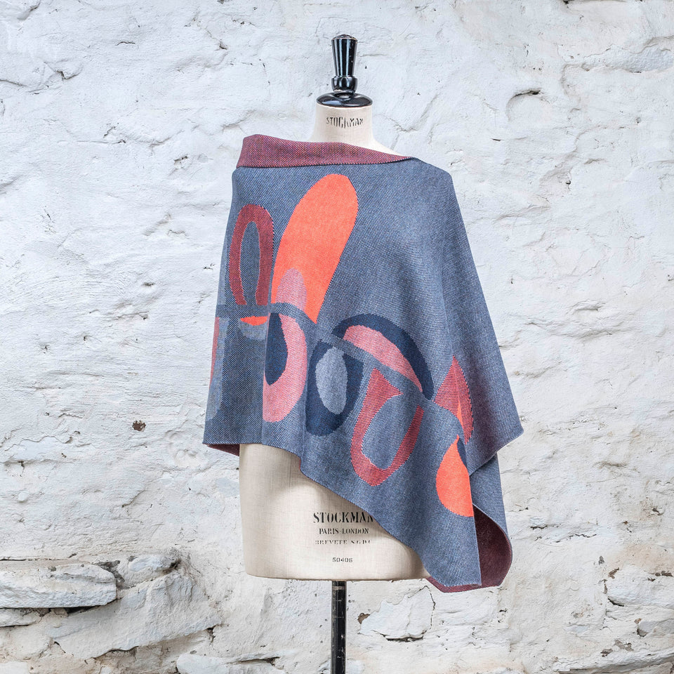 Knitted cape in blues with accents in coral. The pattern is abstract