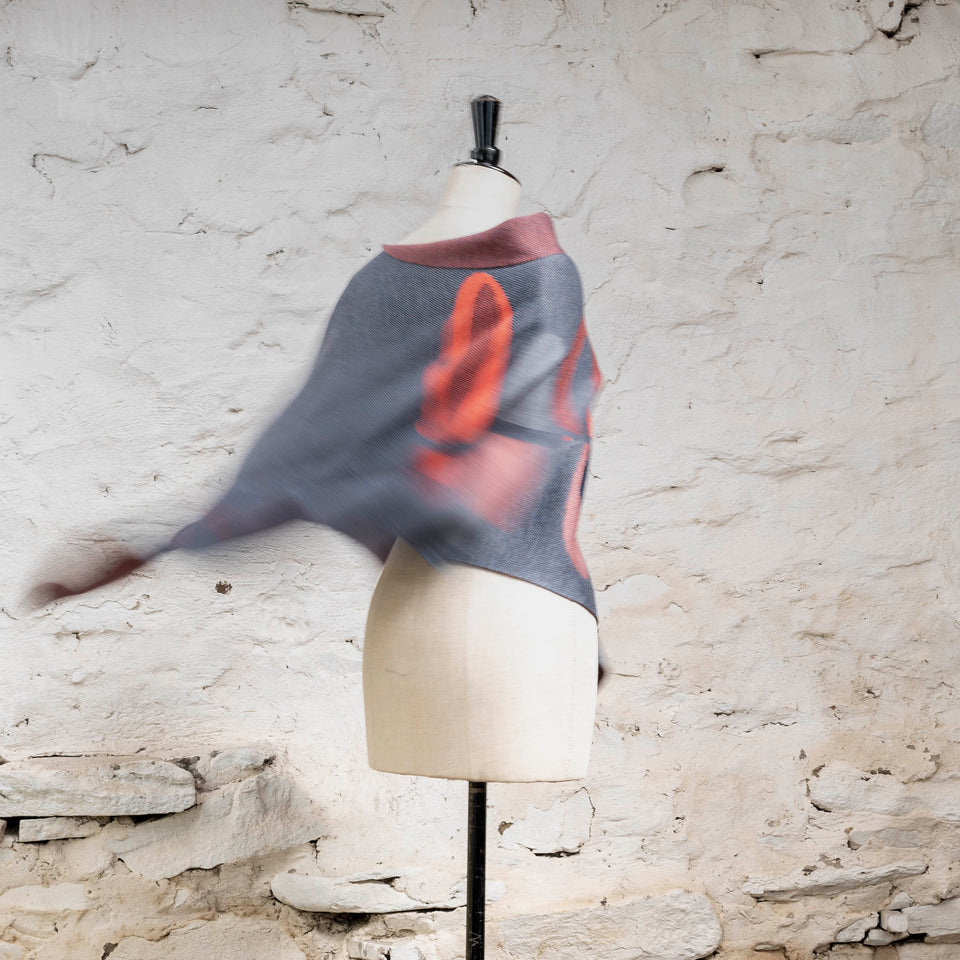 Knitted cape in blues with accents in coral. The pattern is abstract