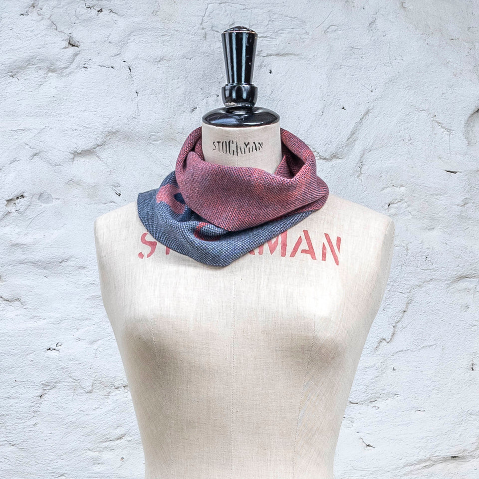 Knitted cowl in blues with accents in coral. The pattern is abstract