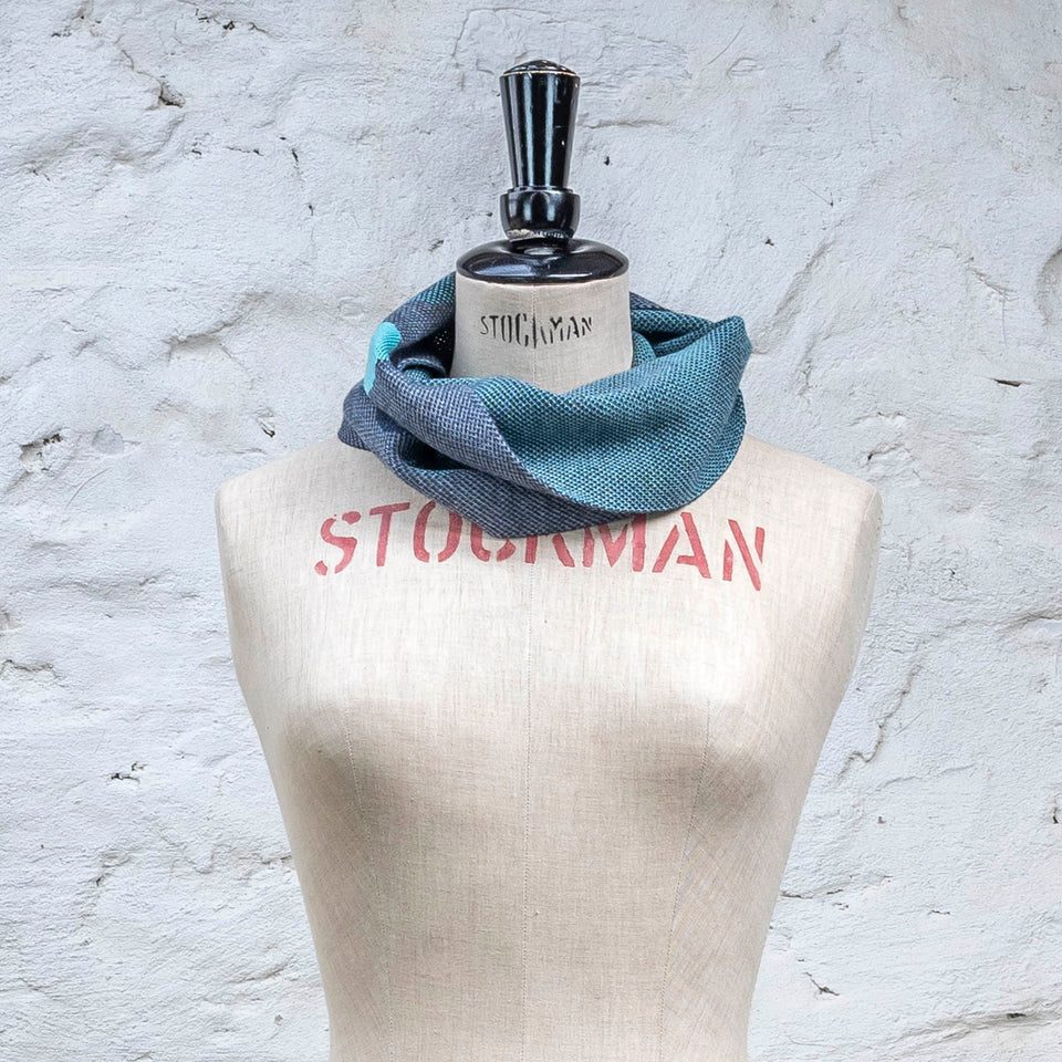 Knitted cowl in blues with accents in aqua. The pattern is abstract