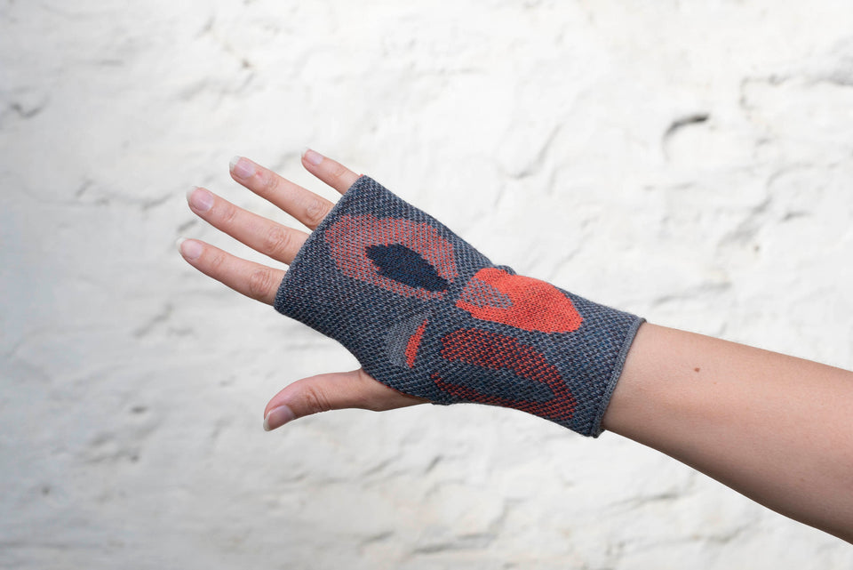 Knitted gauntlet mitts in blues with accents in coral. The pattern is abstract