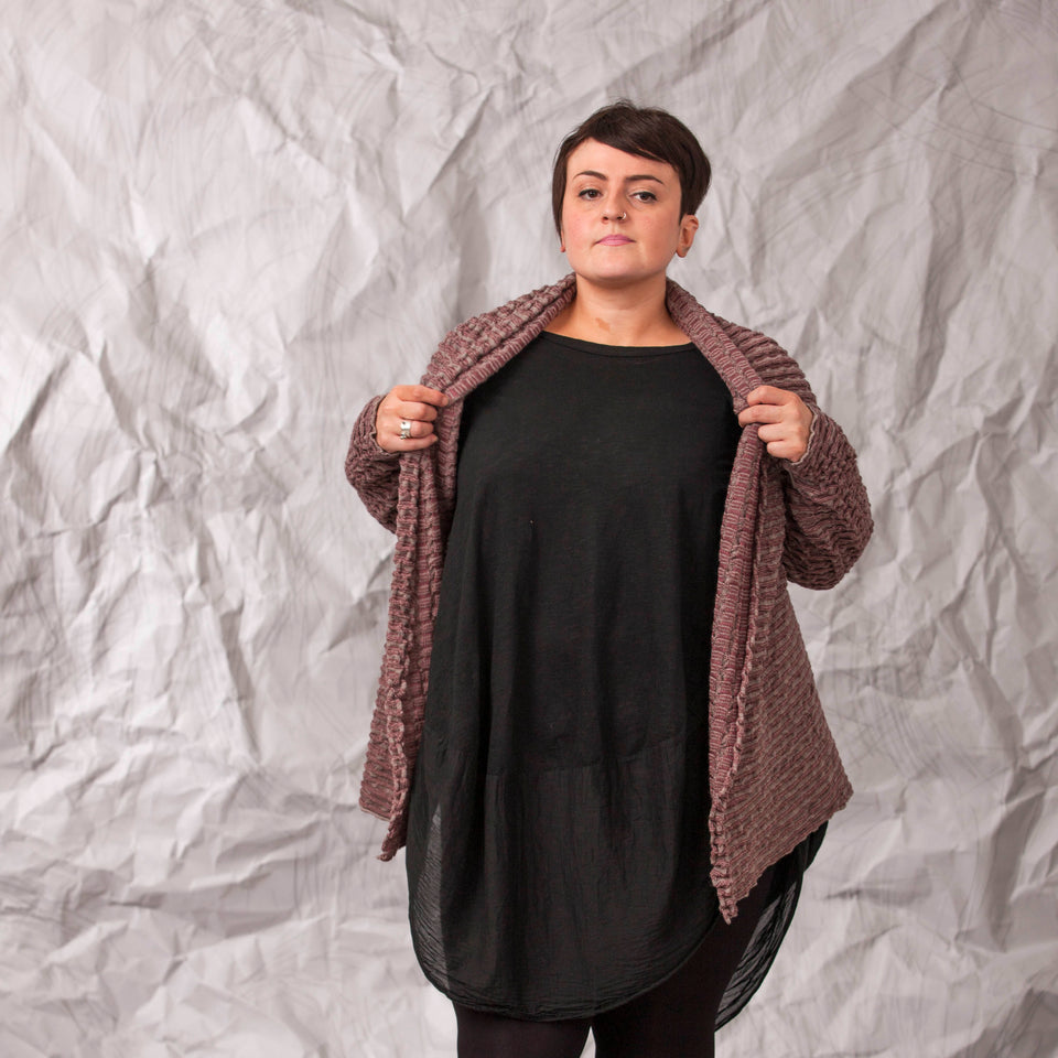 Model wears a longline knitted contemporary jacked in ridged fabric, in warm beige and cherry. Front view, with jacket open to show neck