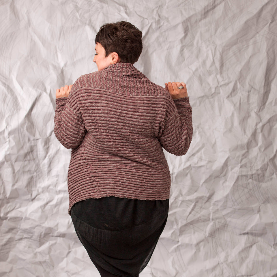 Model wears a longline knitted contemporary jacked in ridged fabric, in warm beige and cherry. Rear view with jacket closed