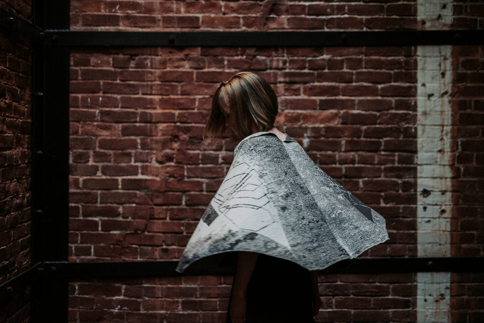 Knitted Byre cape. Abstract, graphic design in an asymmetric shape. Shown in Charcoal and stone white