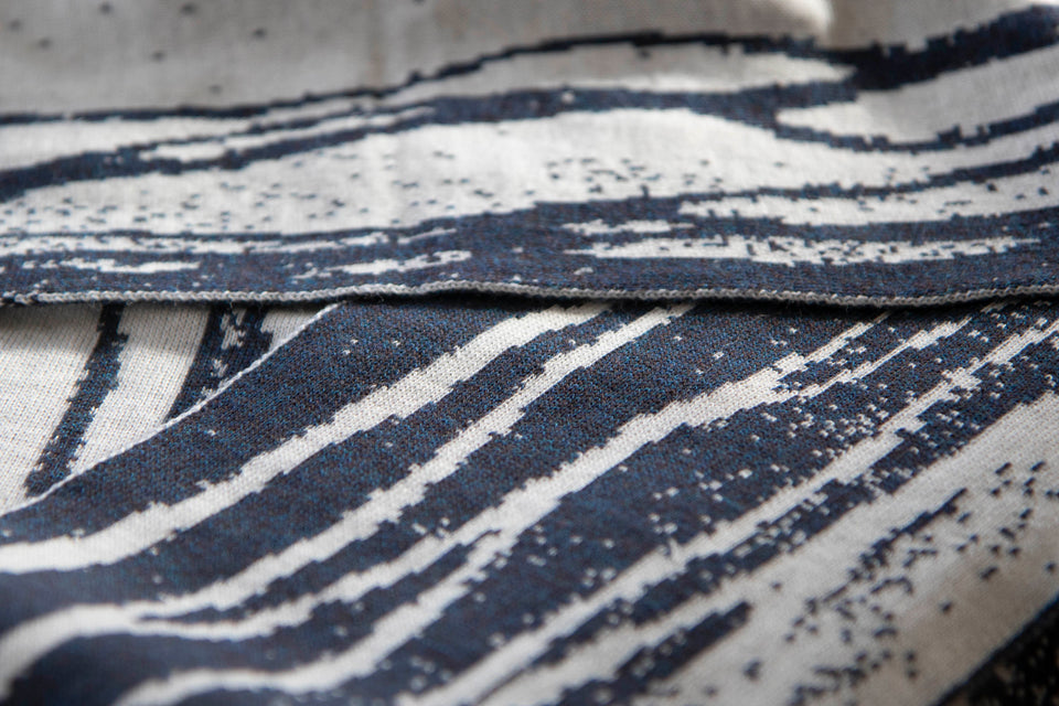 close up view of shoormal scarf showing the speckled and finely knitted fabric and the smoky blue yarn - a marl - against the off white.