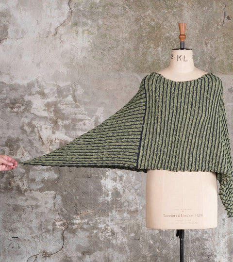 A ridged, knitted cape is shown on a vintage mannequin. Knitted in green, the side is pulled out to show the stretch in the garment.