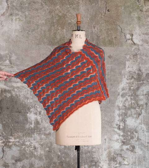 Modern Shetland lace cape on a vintage mannequin. Knitted in rusts and blues. Shown against an old Shetland wall