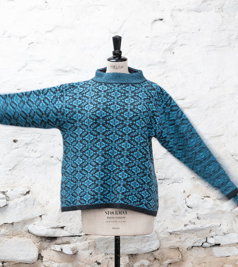 Shetland Fair Isle jumper in blues with all-over pattern. Shown on a vintage mannequin against a whitewashed, rustic stone wall.