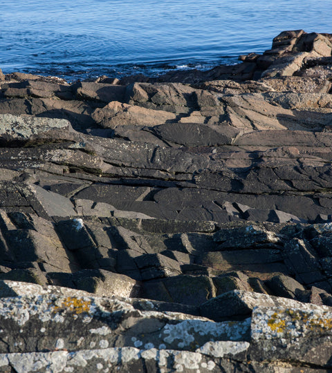 At hoswick, Shetland rocks are lit by sunlight, with deep blue sea in the background